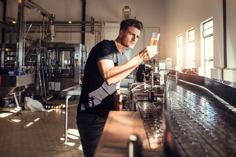 A brewer checking a tank by hand.