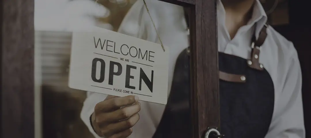 A hand turning the sign in the door to OPEN.